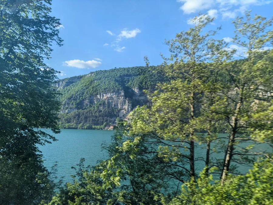 A turquoise lake (Lac de Nantua) in front of a forest-covered mountain